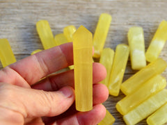 One small yellow calcite crystal tower 65mm on hand with background with some crystals on wood table