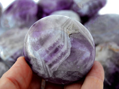 One amethyst crystal palm stone 50mm on hand with background with some crystals inside a basket