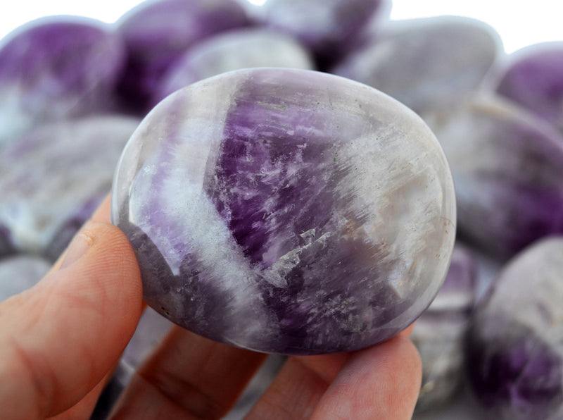 One amethyst crystal palm stone 40mm on hand with background with some crystals inside a basket