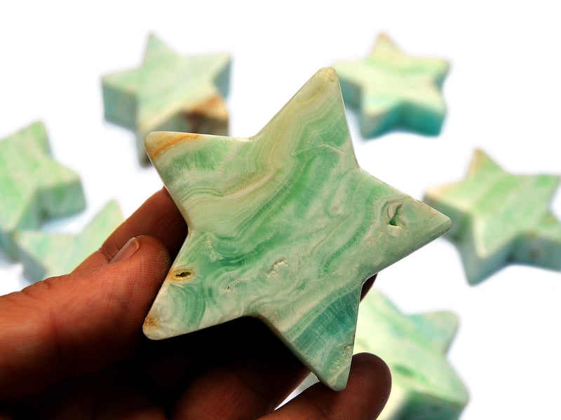 One blue caribbean calcite star crystal 60mm on hand with background with some stars on white