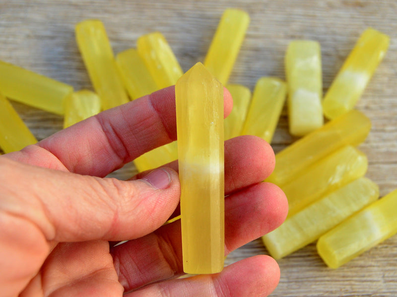 One small yellow calcite tower point 60mm on hand with background with some crystals on wood table