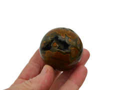 One green and mustard yellow ocean jasper sphere 40mm on hand with white background