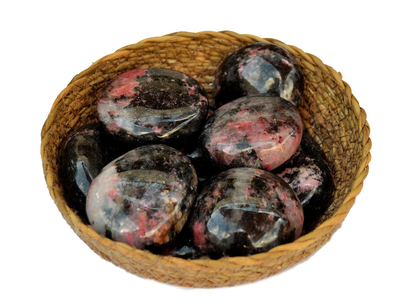 Some rhodonite palm stones inside a straw basket on white background