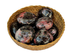 Some rhodonite palm stones inside a straw basket on white background