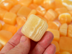 One orange calcite tumbled mineral 20mm on hand with background with several crystals