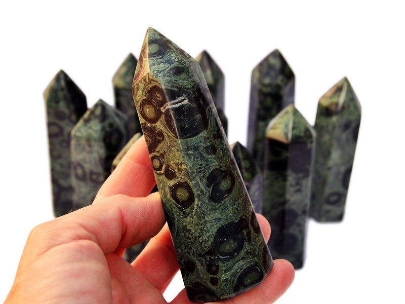 One kambaba jasper obelisk crystal on hand with background with some towers on white