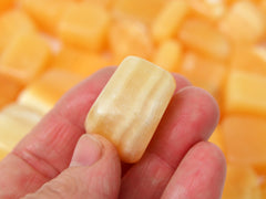 One orange calcite tumbled crystal 20mm on hand with background with several crystals