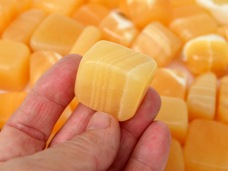 One orange calcite mini tumbled stone  20mm on hand with background with several crystals