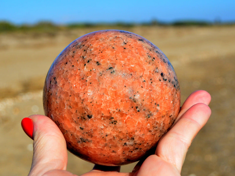 Orange calcite crystal sphere 80mm on hand with sand background