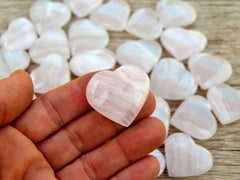 One mini pink mangano calcite crystal heart 30mm on hand with background with several hearts on wood table