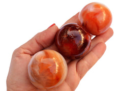 Three carnelian mineral spheres 50mm-60mm on hand with white background