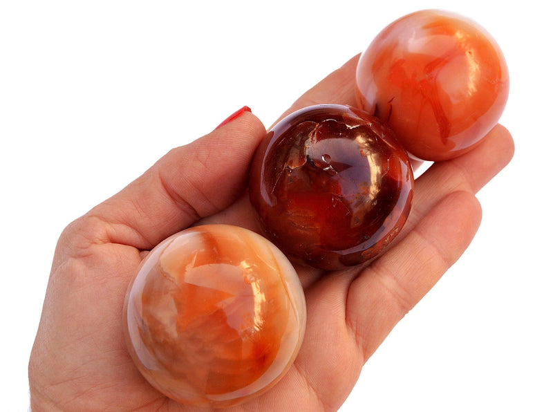 Three carnelian crystal spheres 50mm-55mm on hand with white background