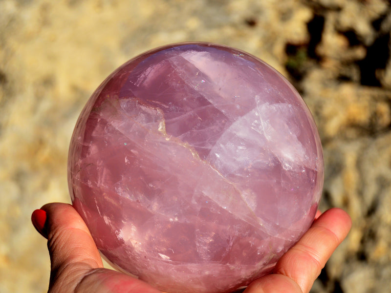 One large rose quartz crystal sphere 100mm on hand with rock background 