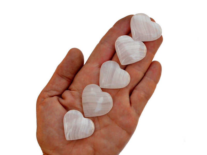 Five small pink mangano calcite crystal hearts 30mm-35mm on hand with white background