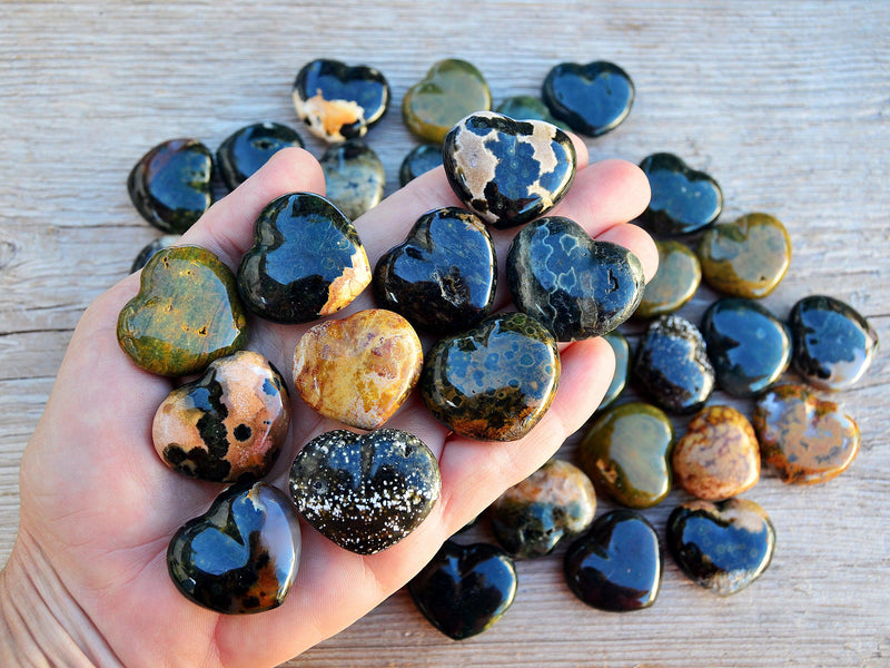 Ten ocean jasper heart crystals 30mm on hand with background with some hearts on wood table