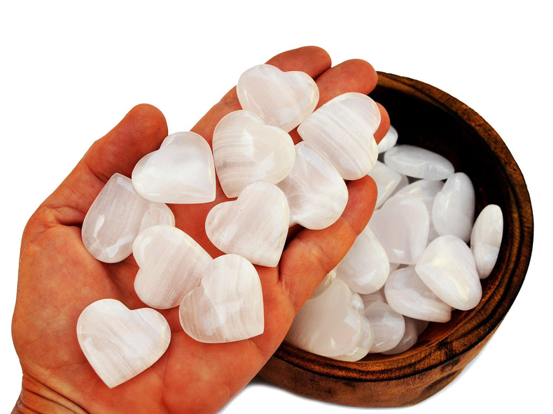 Ten pink mangano calcite crystal hearts 30mm-35mm on hand with background with some hearts inside a wood bowl on white