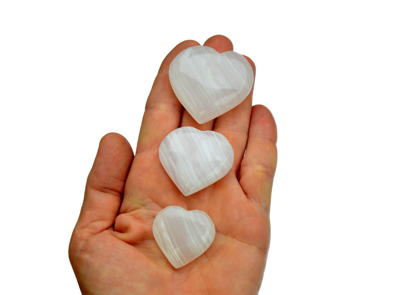 Three small mangano calcite crystal hearts 25mm-40mm on hand with white background