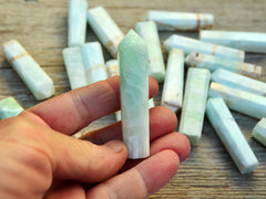 One mini blue calcite caribbean calcite point crystals 60mm on hand with background with some points on wood table