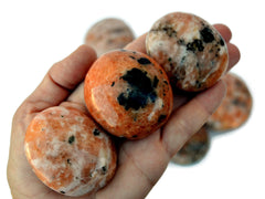 Three orange calcite palm stones 45mm on hand with background with some stones on white