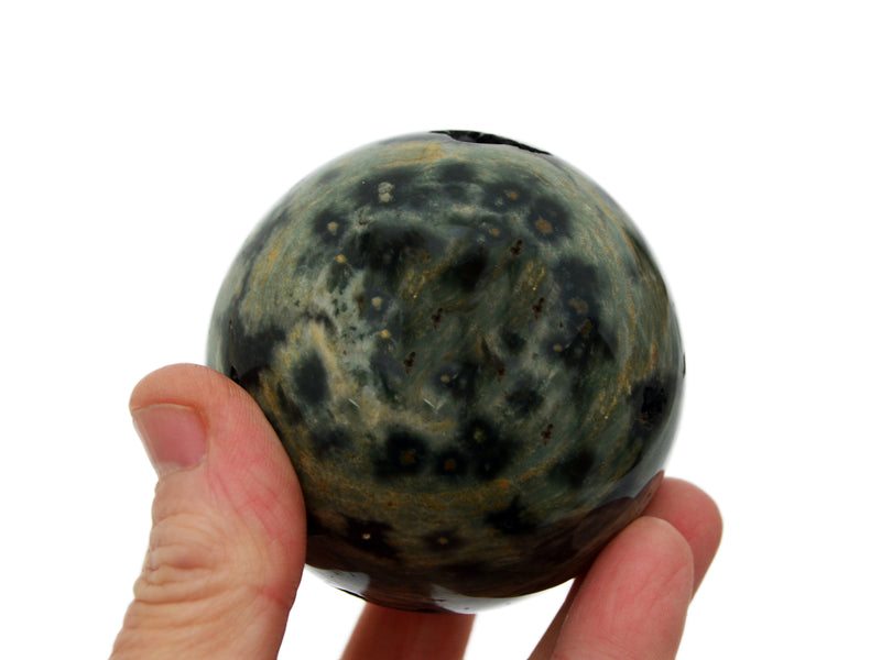 One green and gray ocean jasper sphere 60mm on hand with background with some spheres on white