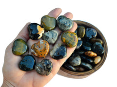 Ten ocean jasper heart crystals 30mm on hand with  background with some stones inside a wood bowl