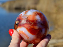 One white and orange carnelian crystal ball 80mm on hand with river landscape background