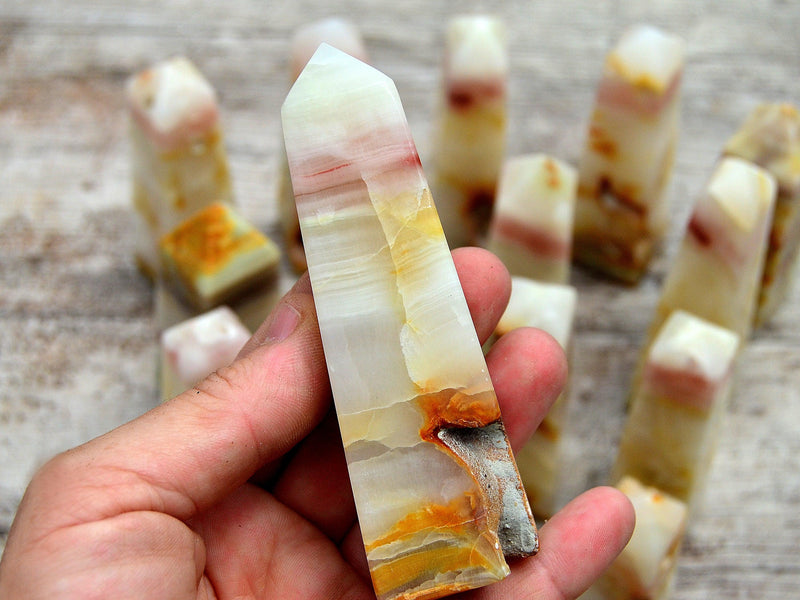 One big pink banded onyx obelisk stone on hand with background whit some crystals on wood table