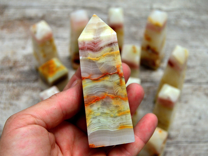 One chunky pink banded onyx tower on hand with background whit some stones on wood table
