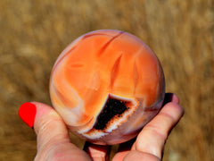 One natural carnelian crystal ball 70mm on hand with straw landscape background