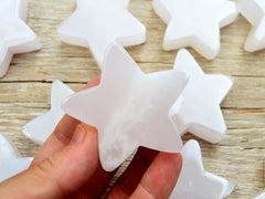 One pink mangano calcite star 60mm on hand with background with some star stones on wood table