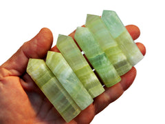 Six small pistachio calcite faceted crystal points on hand on white background
