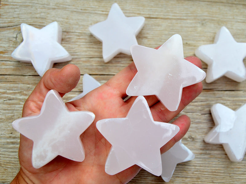 Three pink mangano calcite stars 60mm on hand with background with some star stones on wood table