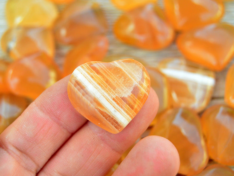 One small banded honey calcite heart crystal 25mm on hand with background with several hearts on wood table