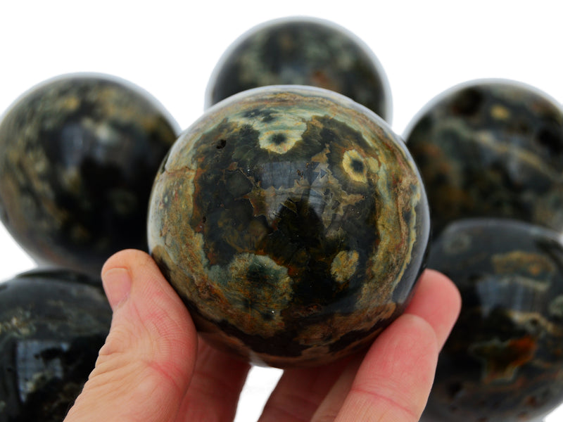 One green and brown ocean jasper sphere stone 55mm on hand with white background