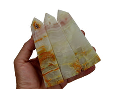 Three large pink banded onyx crystal obelisks on hand with white background