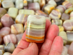 One pink banded onyx tumbled stone on hand with background with several crystals