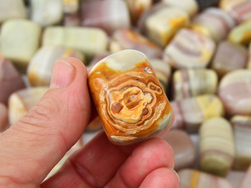 One pink banded onyx tumbled mineral on hand with background with several specimens