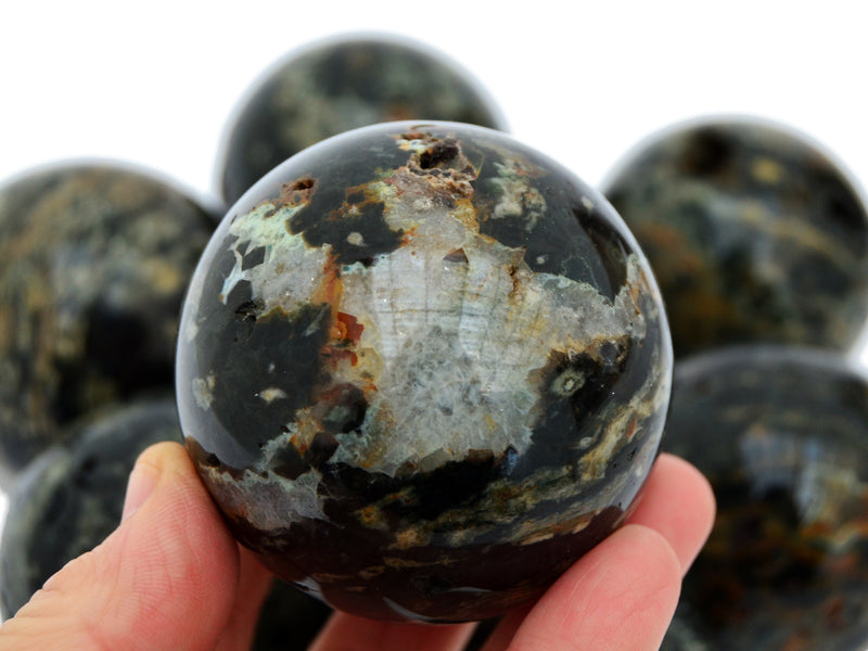 One green ocean jasper sphere 60mm on hand with background with some spheres on white