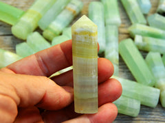 One pistachio calcite prism 55mm on hand with background with some stones on wood table