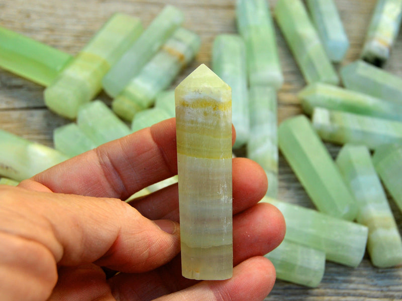 One banded pistachio calcite point crystal 50mm on hand with background with some points on wood table