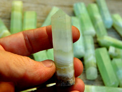 One pistachio calcite prism 60mm on hand with background with some stones on wood table