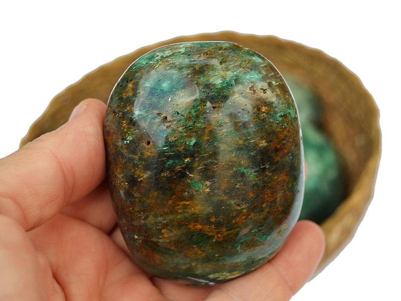 One chrysocolla palm stone 60mm on hand with background with some crystals inside a basket