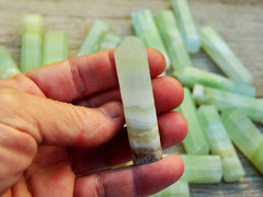One pistachio calcite point crystal 55mm on hand with background with some points on wood table