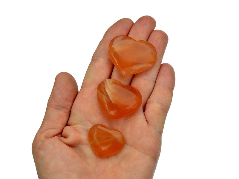 Three honey calcite hearts 25mm-40mm on hand with white background