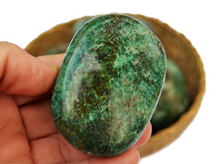 One chrysocolla palm stone 70mm on hand with background with some crystals inside a basket