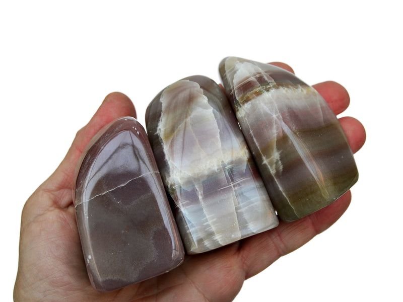 Three pink banded onyx free form stones 60mm-70mm on hand with white background