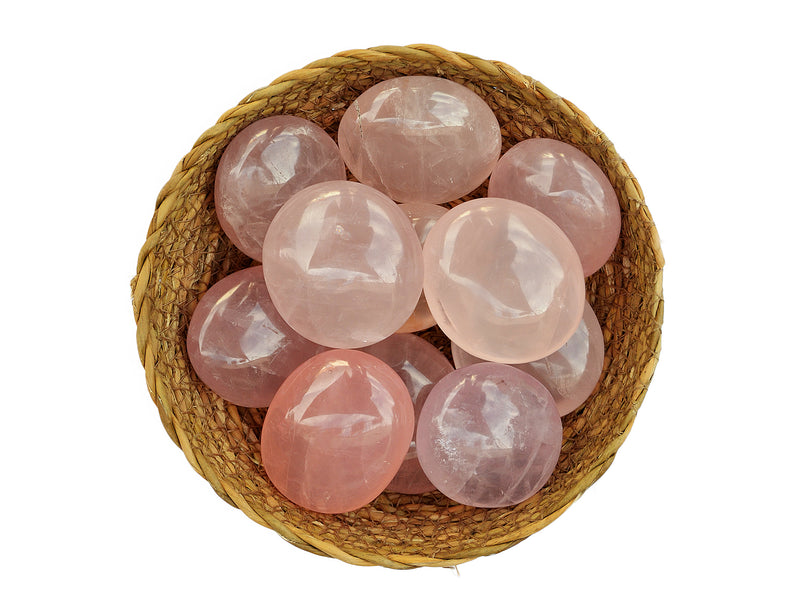 Several rose quartz palm stones 40mm - 70mm inside a straw basket on white background