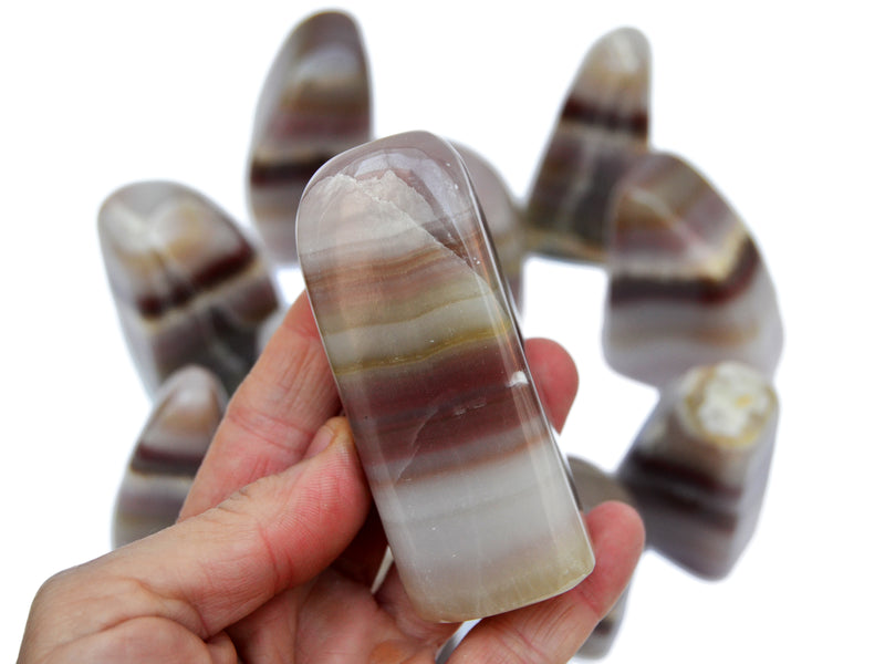 One pink banded onyx crystal free form 90mm on hand with background with some stones on white