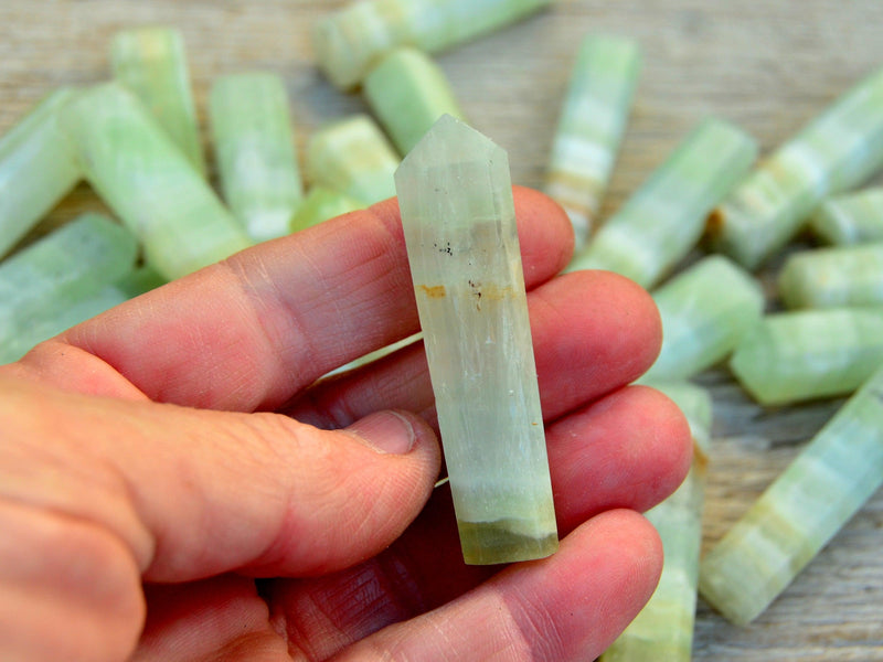 One pistachio calcite faceted crystal point 50mm on hand with background with some points on wood table
