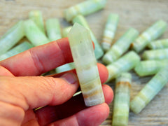 One green pistachio calcite point 50mm on hand with background with some points on wood table